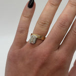 Gold ring with a diamond on a person's finger against a neutral background