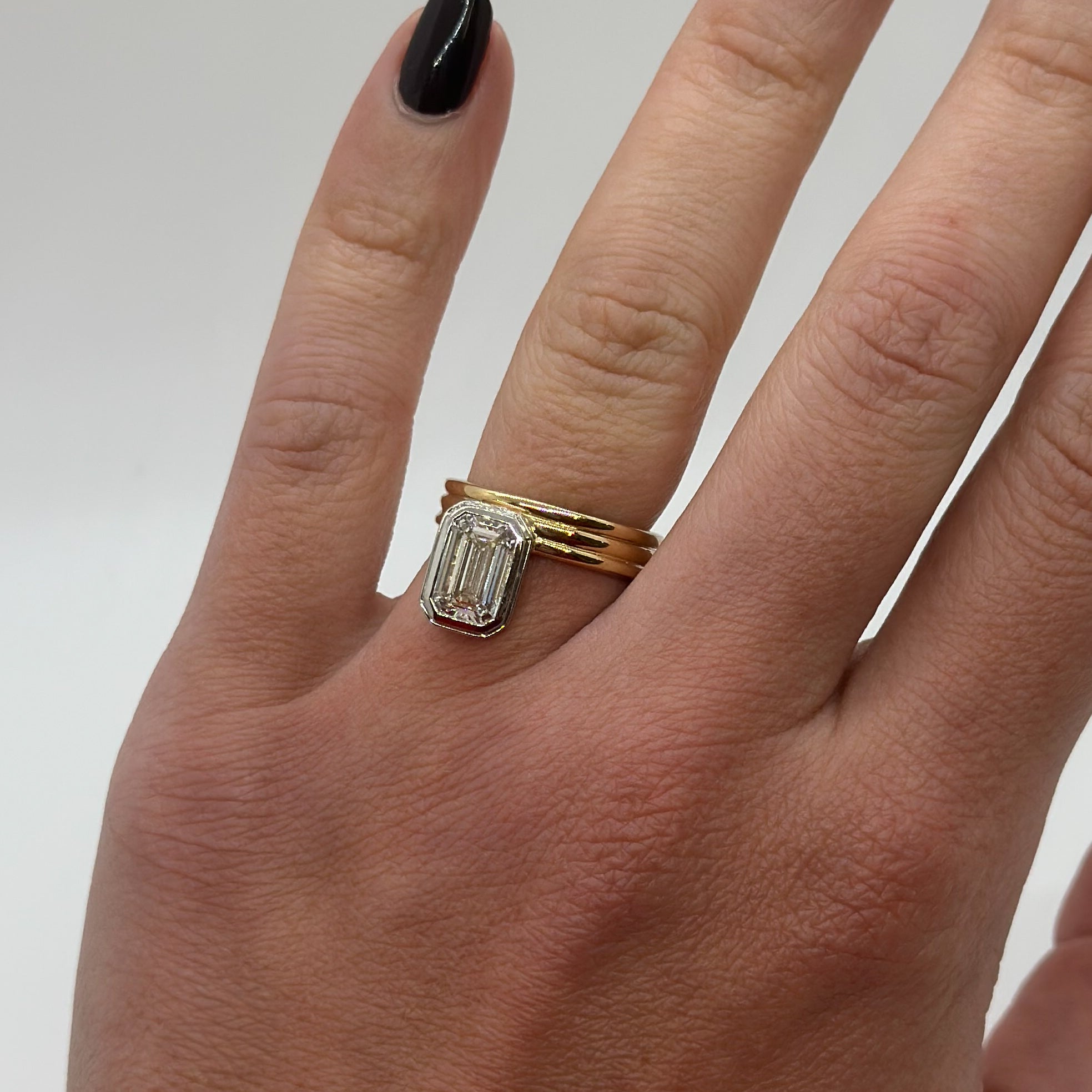 Gold ring with a diamond on a person's finger against a neutral background
