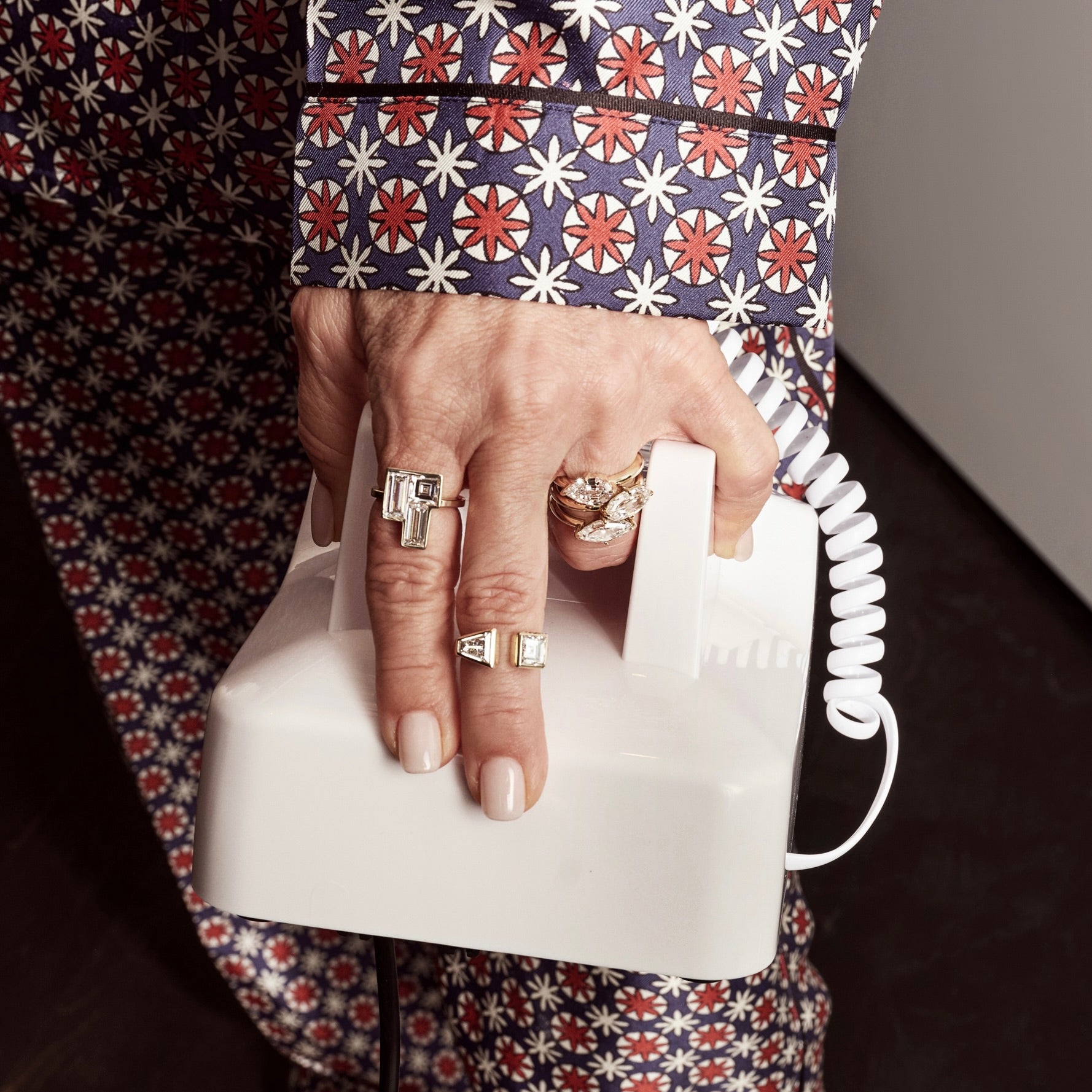 Hand wearing 5 rings by Shahla Karimi made in yellow gold with diamonds holding telephone