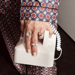 Hand wearing five Shahla Karimi rings made of gold and diamonds holding telephone