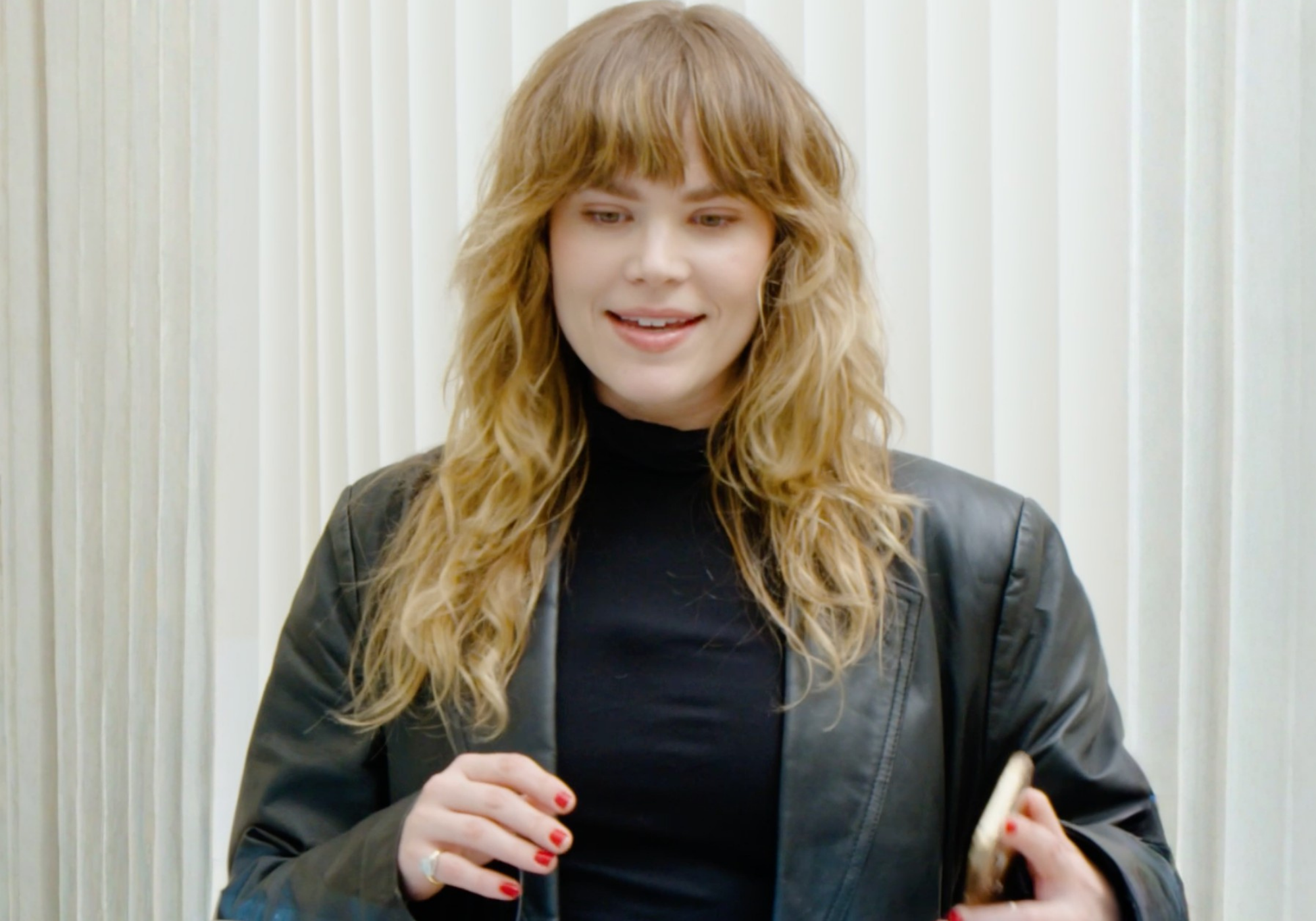 Woman with long blonde hair and a black top against a light background