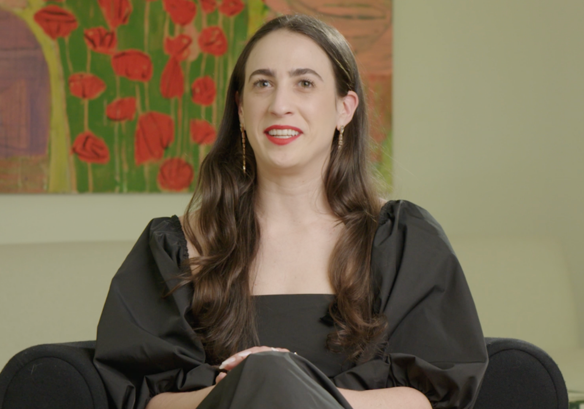 Woman sitting in a room with a painting of red flowers on the wall