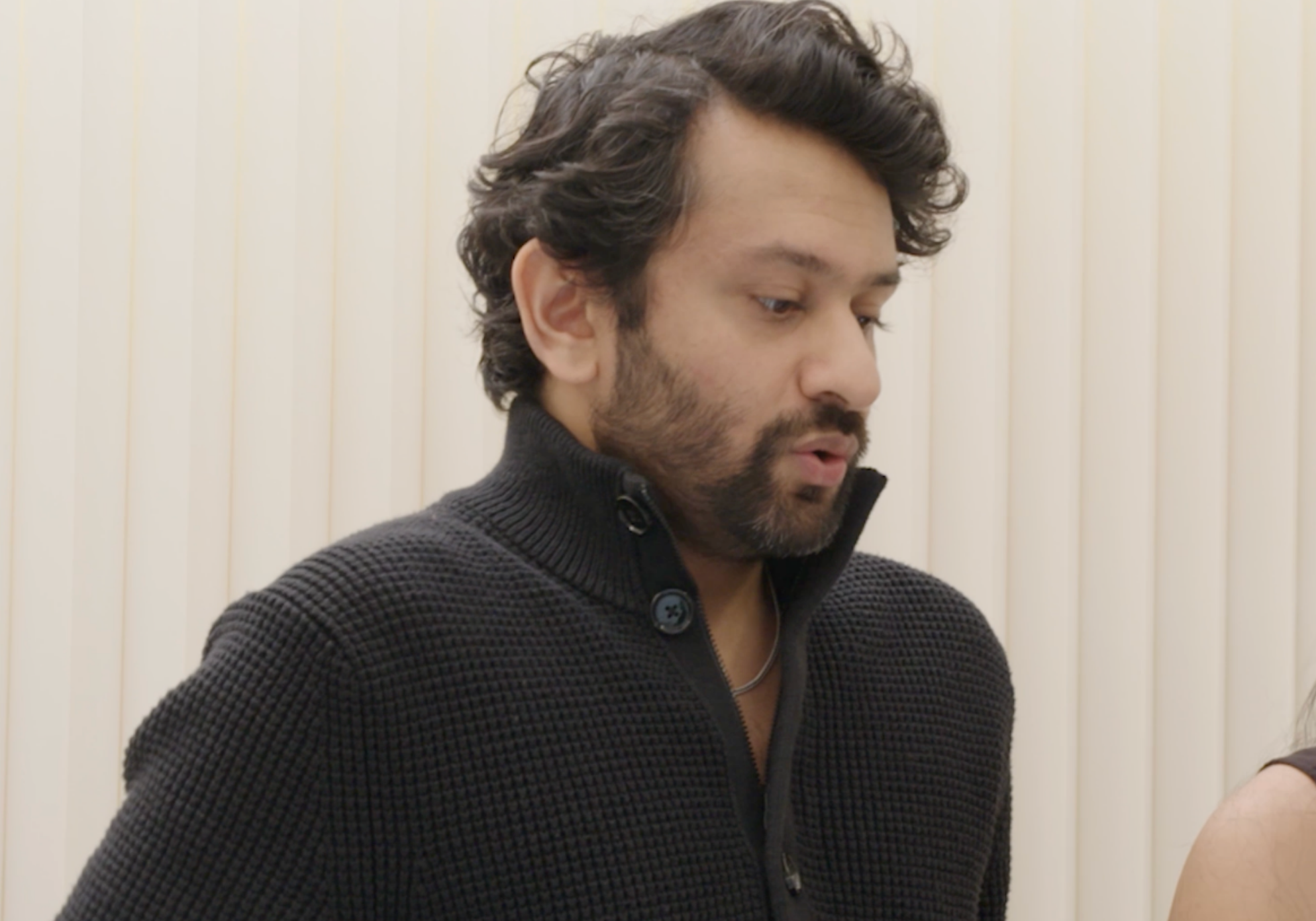 Man wearing a black textured sweater against a neutral background