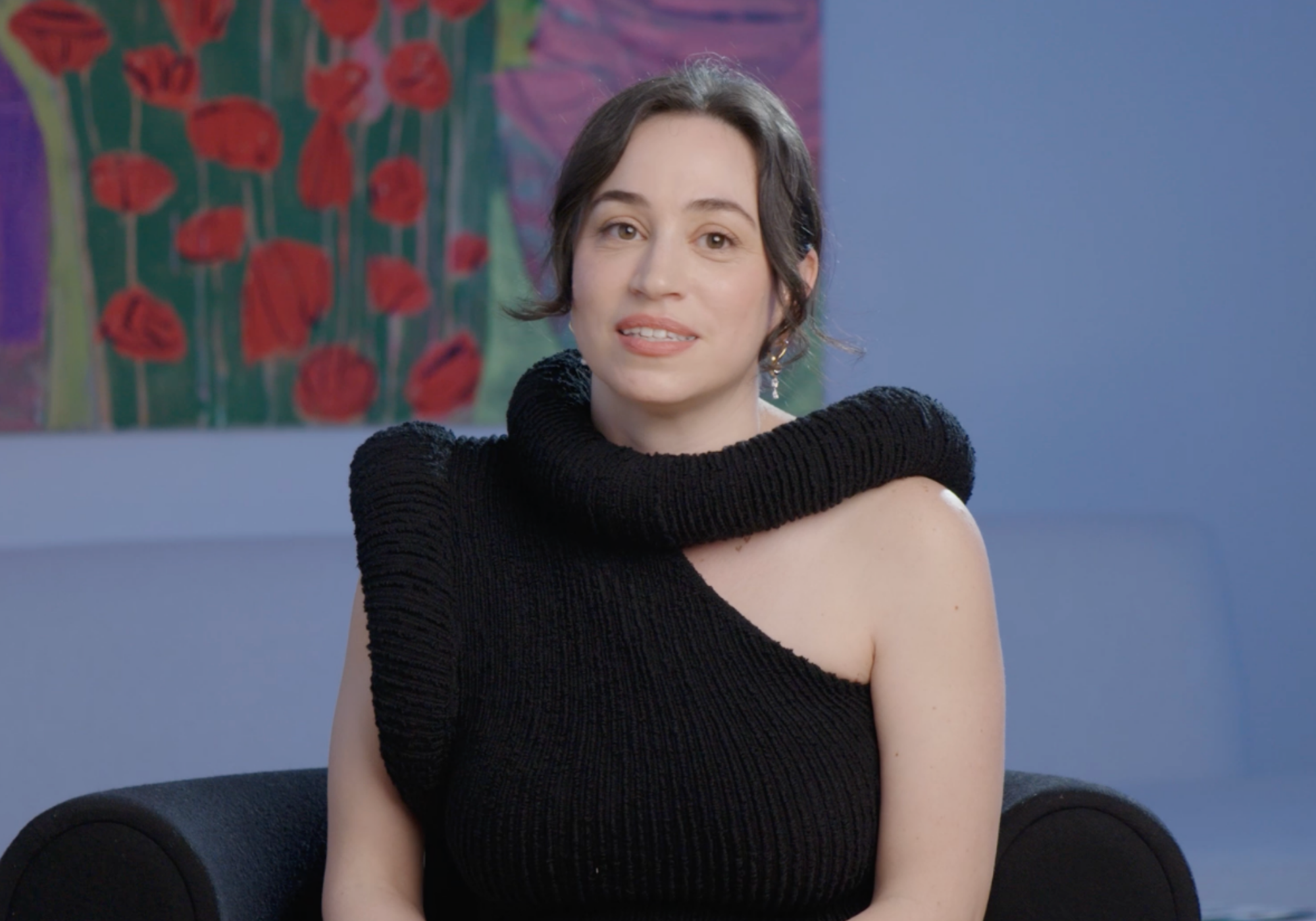Woman wearing a black knit top sitting in a room with colorful abstract art in the background.