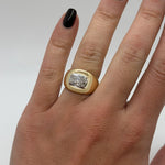 Gold ring with a diamond on a person's finger against a neutral background