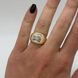 Gold ring with a diamond on a person's finger against a neutral background