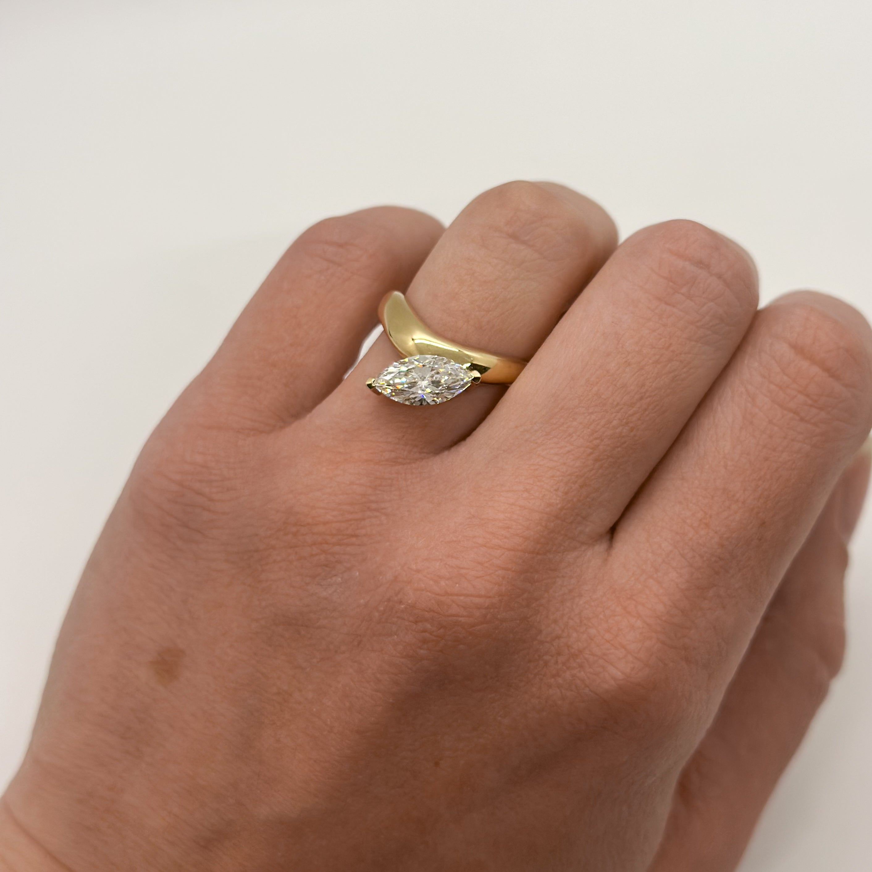 Hand with yellow gold ring and offset marquise-cut diamond on white background