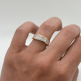 Hand wearing a rose gold ring with baguette diamonds on a plain background