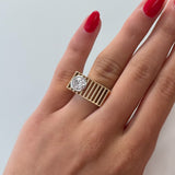 Gold ring with a round diamond on a hand with red nails against a light background