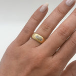 Gold ring with a diamond on a person's ring finger against a neutral background