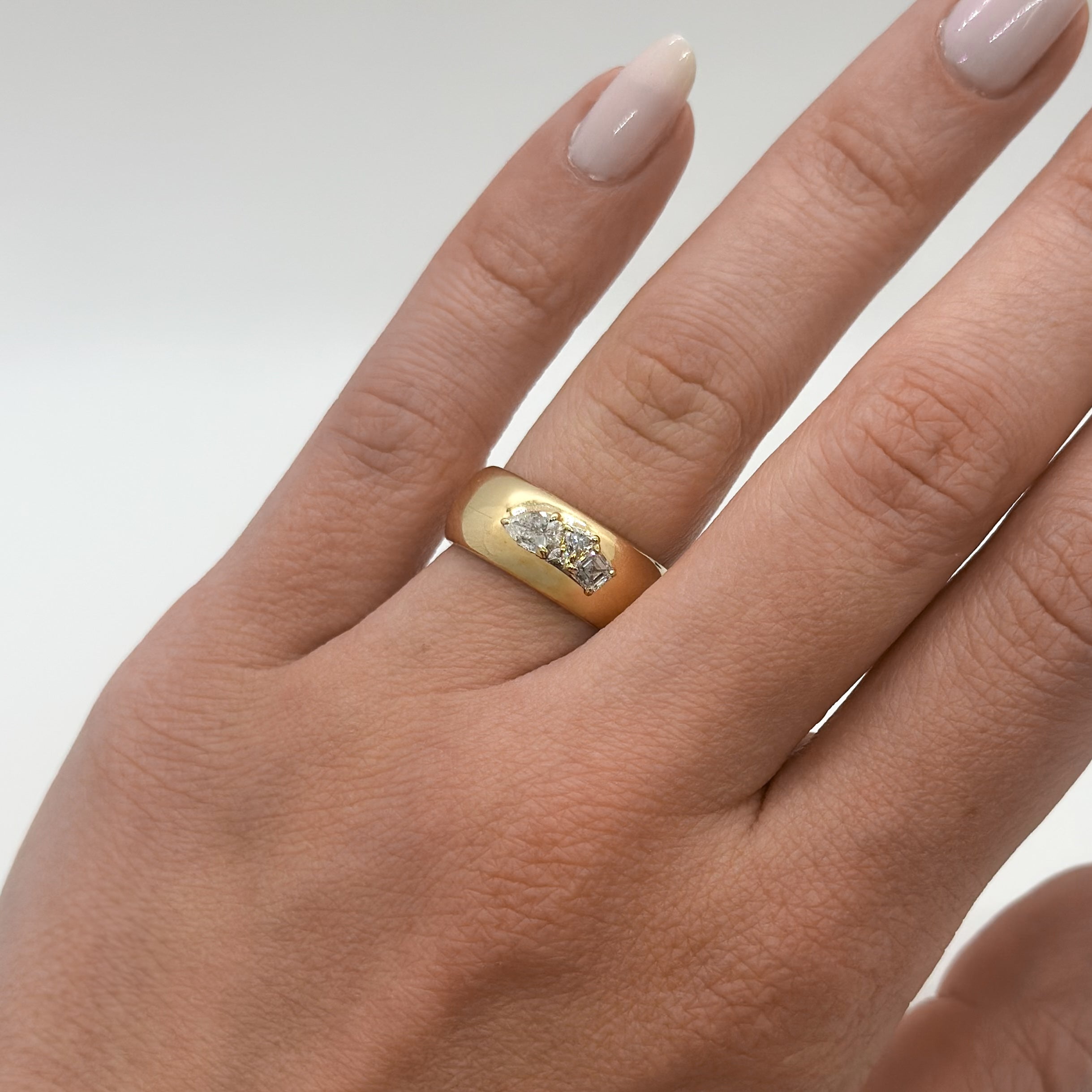 Gold ring with a diamond on a person's ring finger against a neutral background