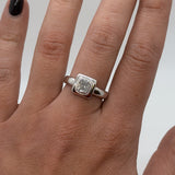 Silver ring with a diamond on a person's finger against a neutral background