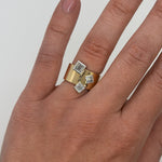 Gold ring with square gemstones on a hand against a white background