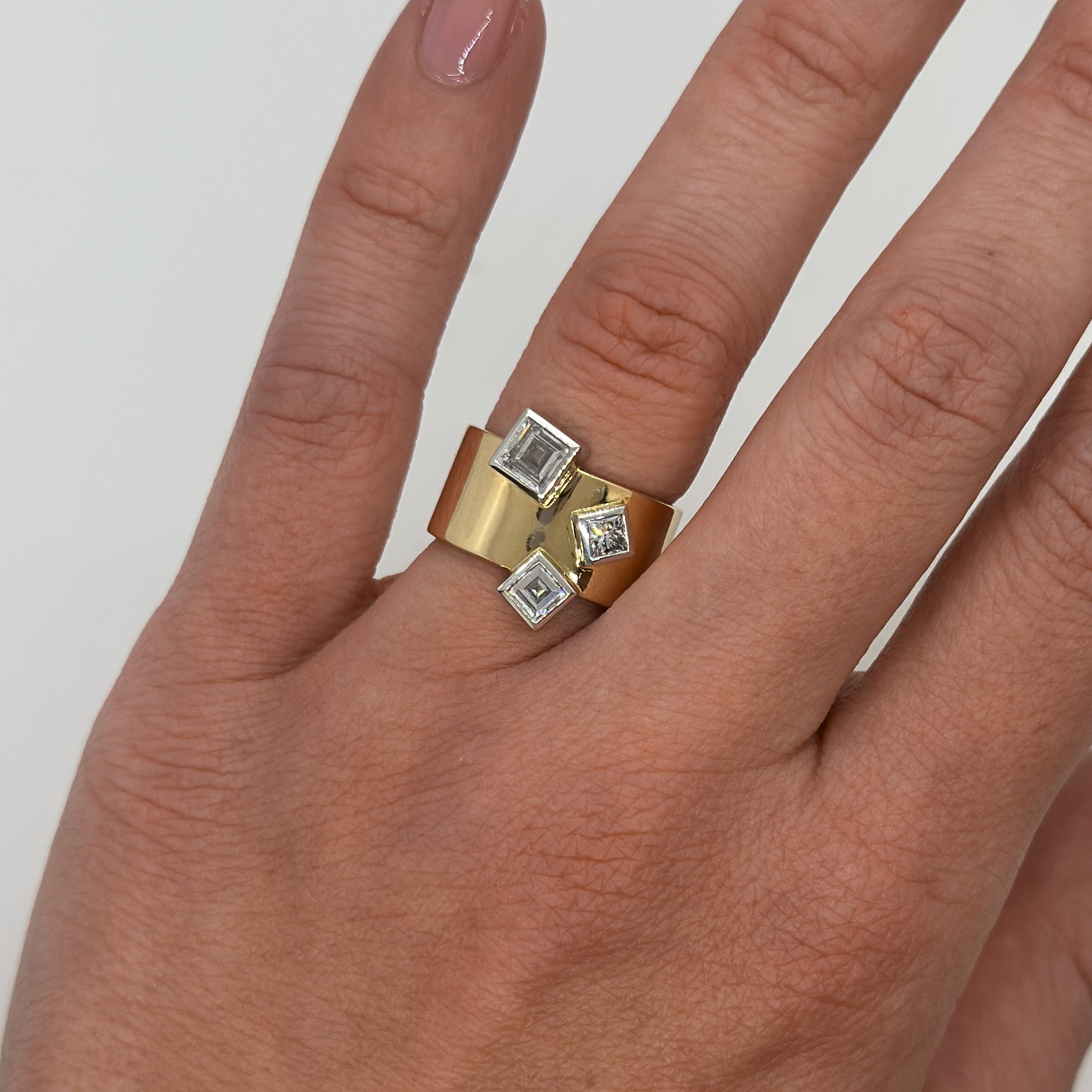 Gold ring with square gemstones on a hand against a white background
