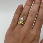 Gold ring with a pear-shaped diamond on a hand against a white background