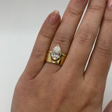 Gold ring with a pear-shaped diamond on a hand against a white background