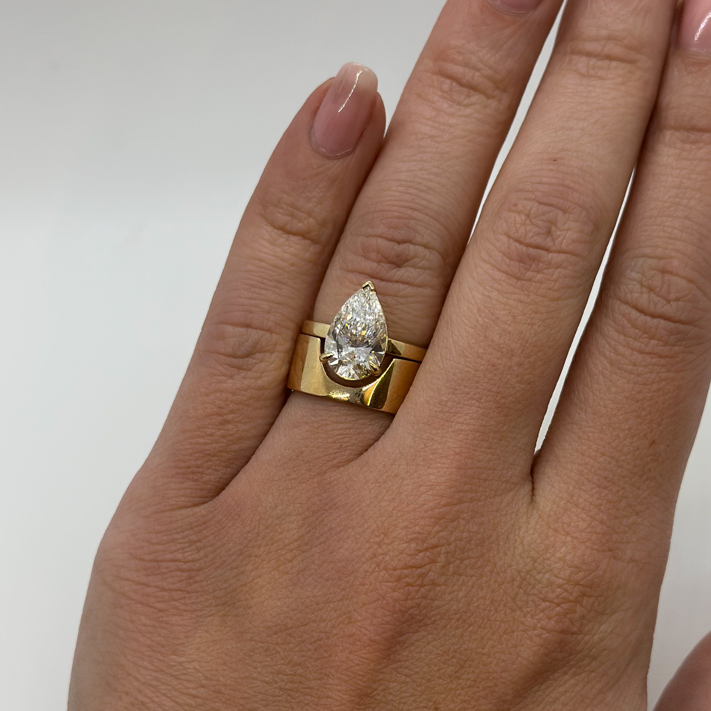 Gold ring with a pear-shaped diamond on a hand against a white background