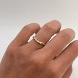 Gold ring with small diamonds on a person's finger against a plain background
