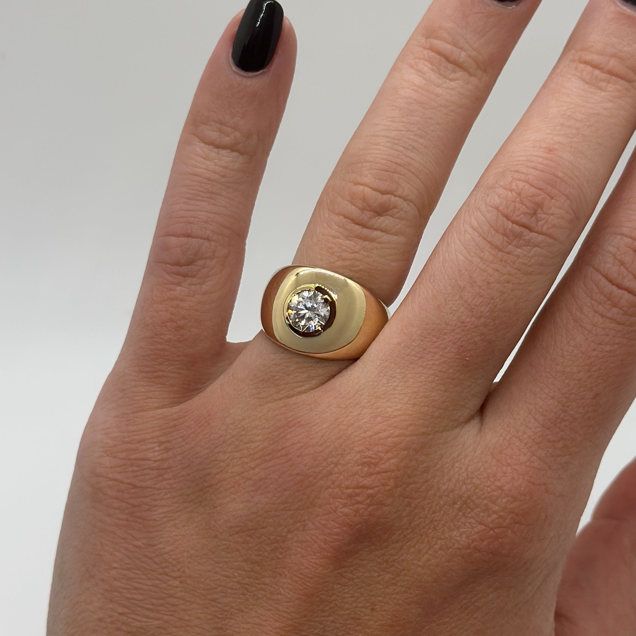 Gold ring with a diamond on a person's finger against a neutral background