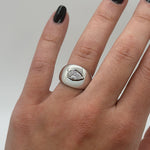 Silver ring with a pear-shaped diamond on a hand against a neutral background