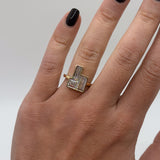 Gold ring with a diamond on a person's finger against a neutral background