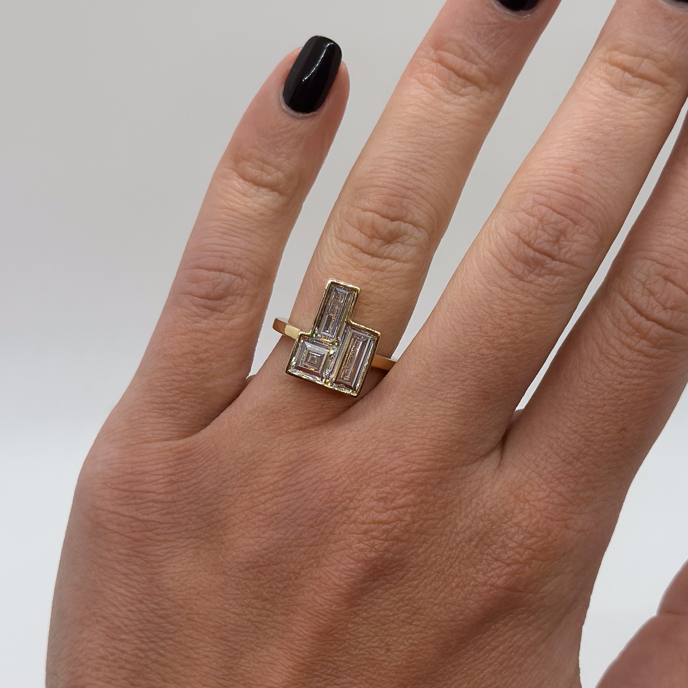 Gold ring with a diamond on a person's finger against a neutral background