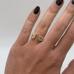 Gold earrings on a hand with black nail polish against a neutral background