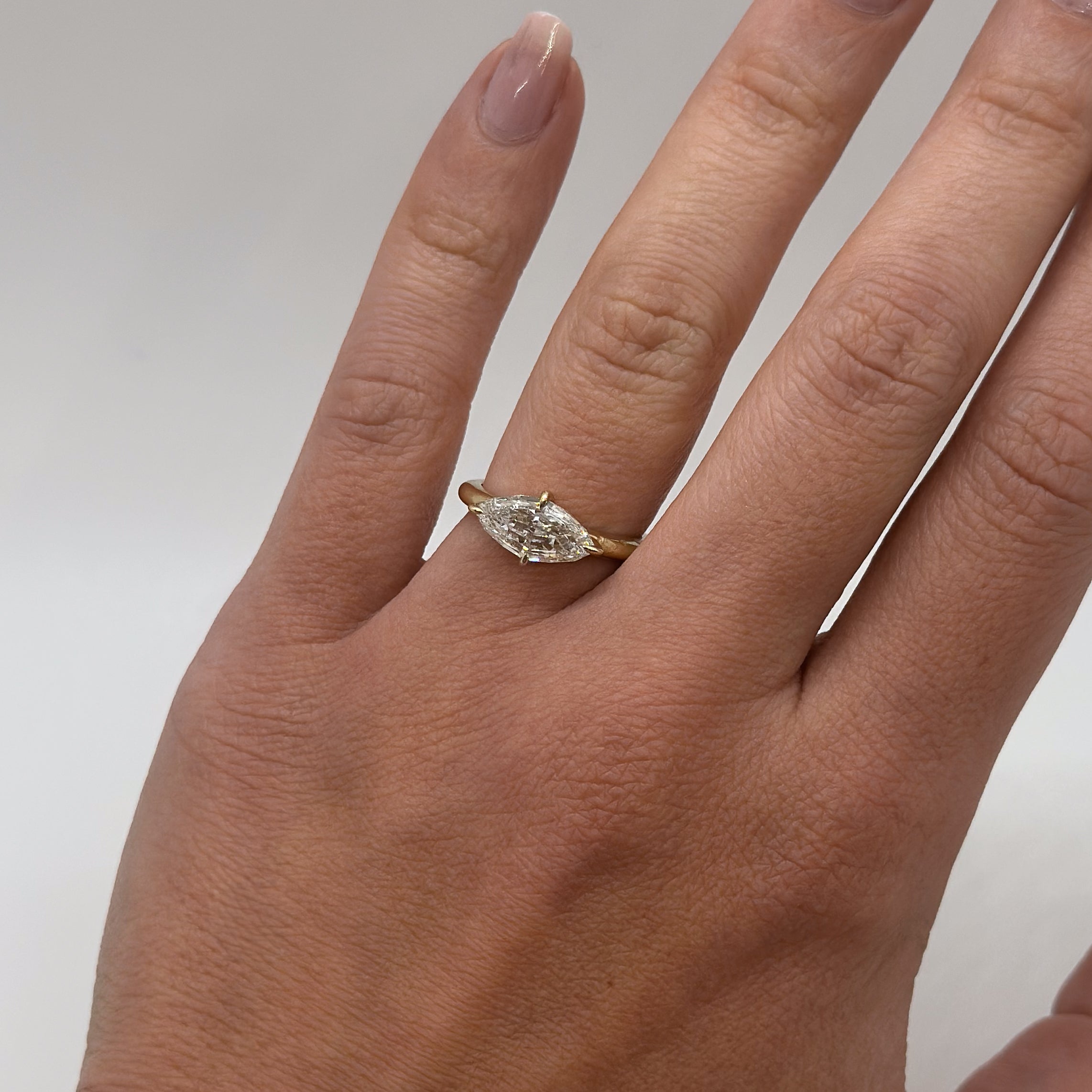 marquise diamond in yellow gold band on hand with neutral background