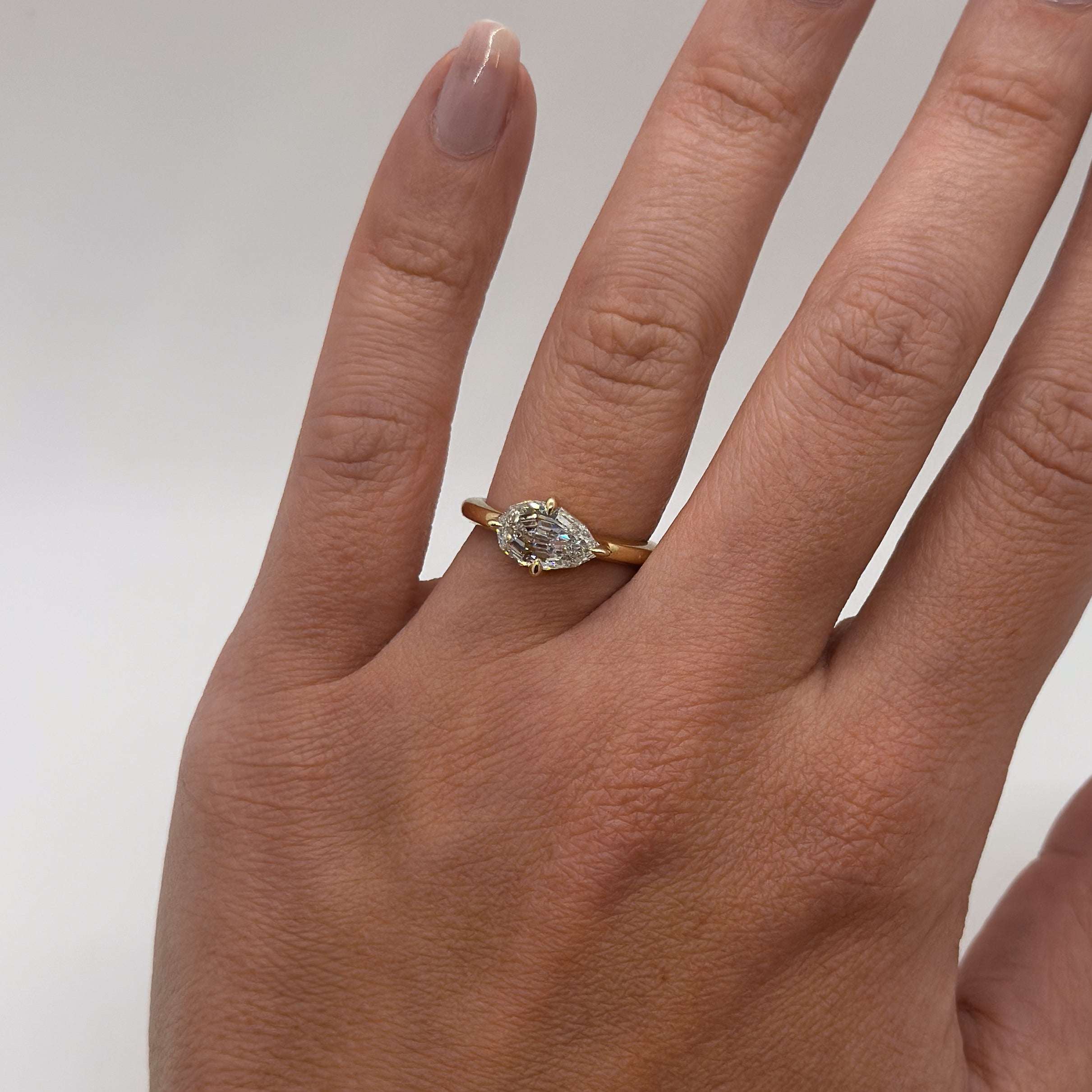 Hand wearing a gold ring with a diamond on a plain background