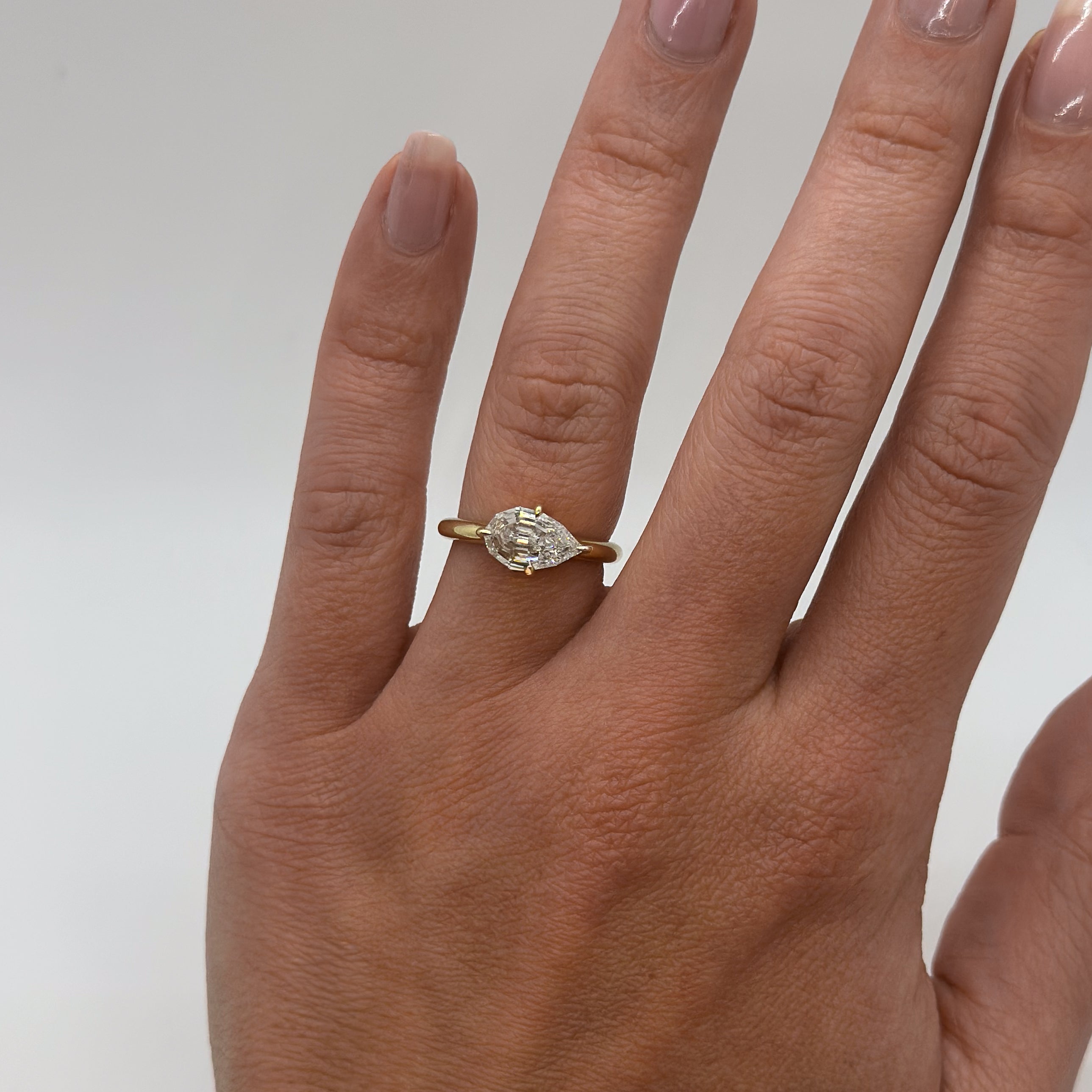 Gold ring with a diamond on a person's finger against a plain background