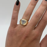 Gold ring with a triangular gemstone on a hand against a neutral background