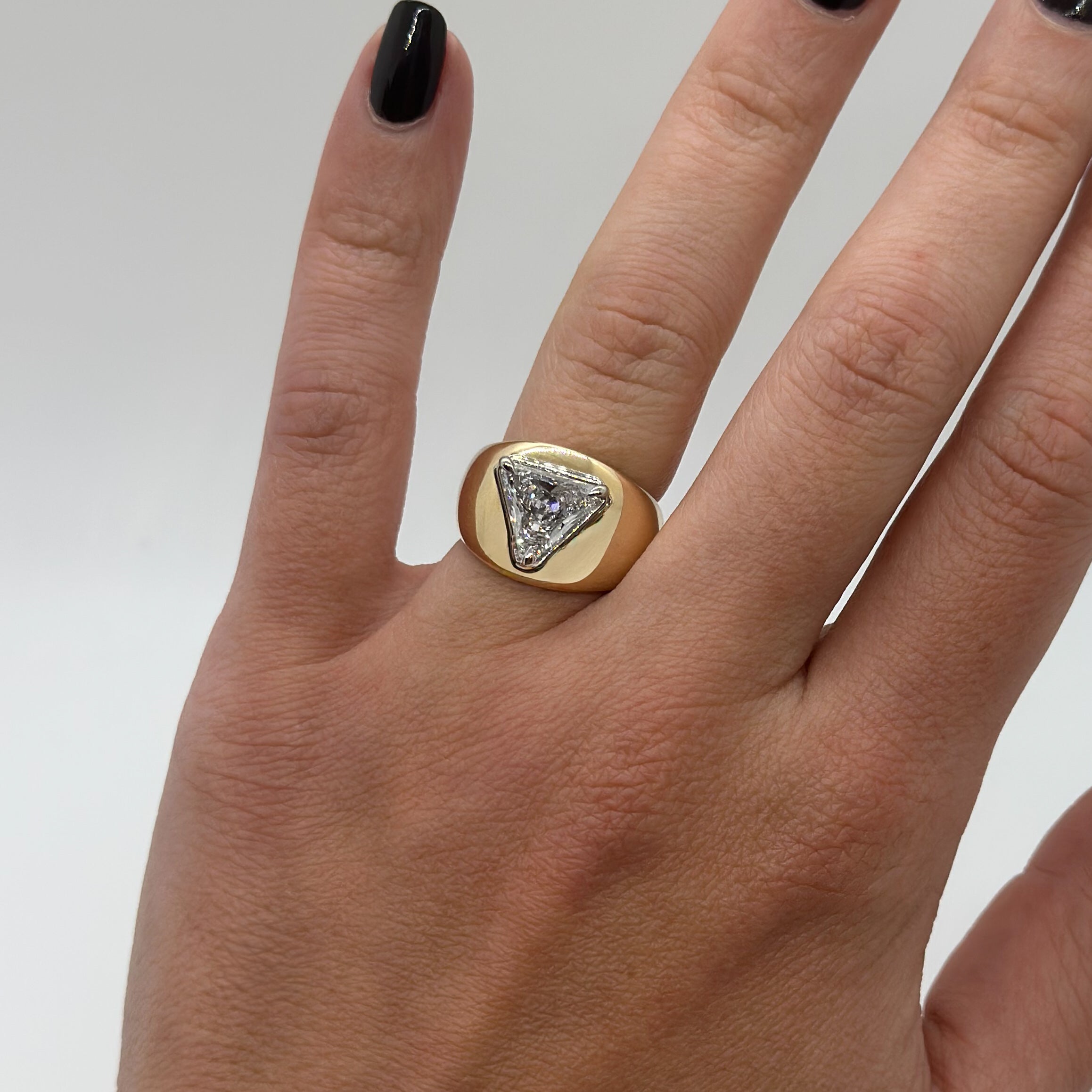 Gold ring with a triangular gemstone on a hand against a neutral background