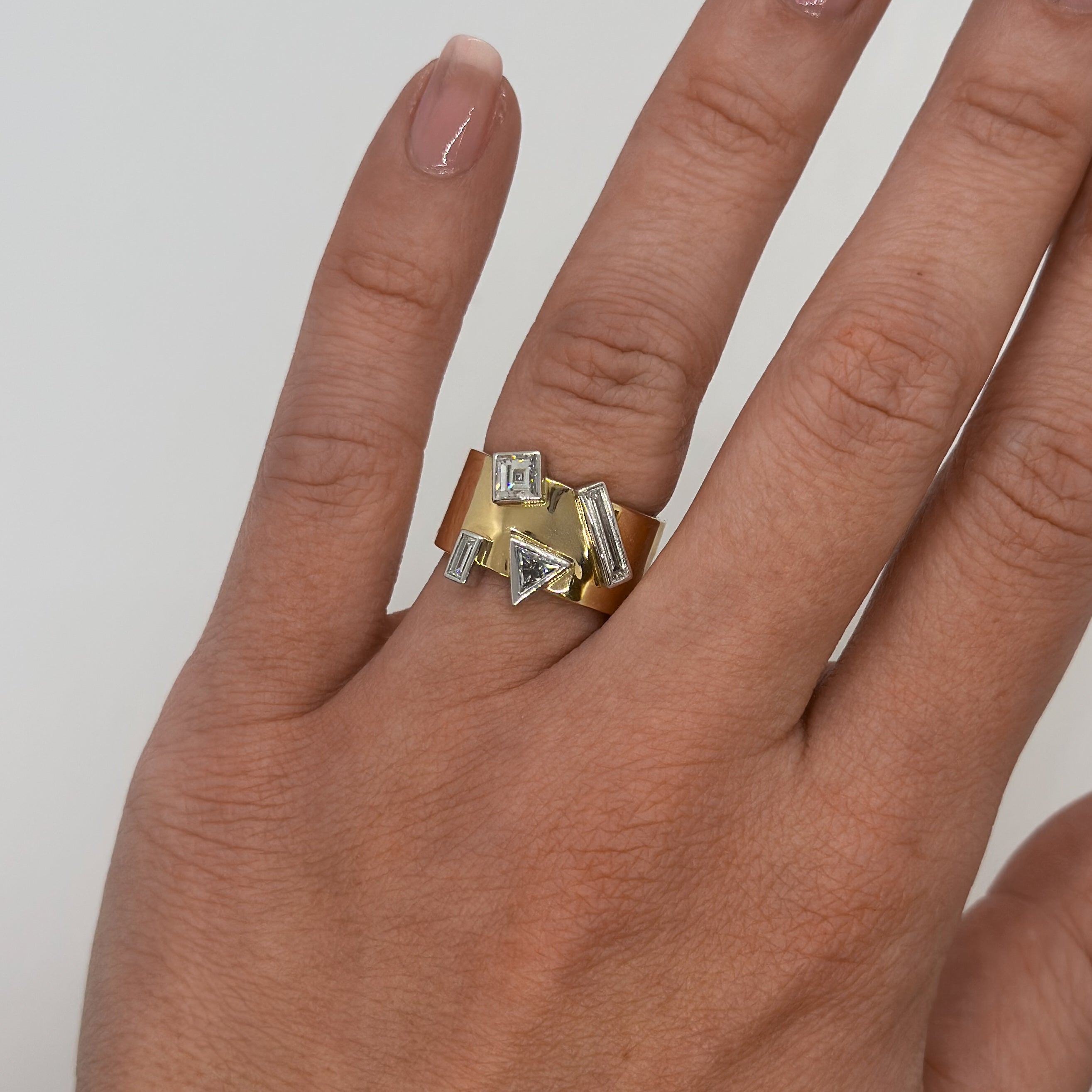Gold ring with geometric design on a finger against a neutral background