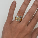 Gold ring with gemstones on a hand against a plain background