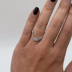 Silver ring with gemstones on a hand with black nail polish against a light gray background