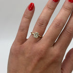 Hand wearing a gold ring with a diamond on a neutral background