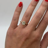 Hand wearing a gold ring with a diamond on a neutral background