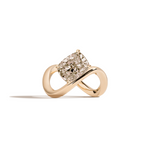 A yellow gold infinity-shaped ring featuring a tilted cushion-cut champagne diamond center stone, set against a clean white background with a soft shadow.
