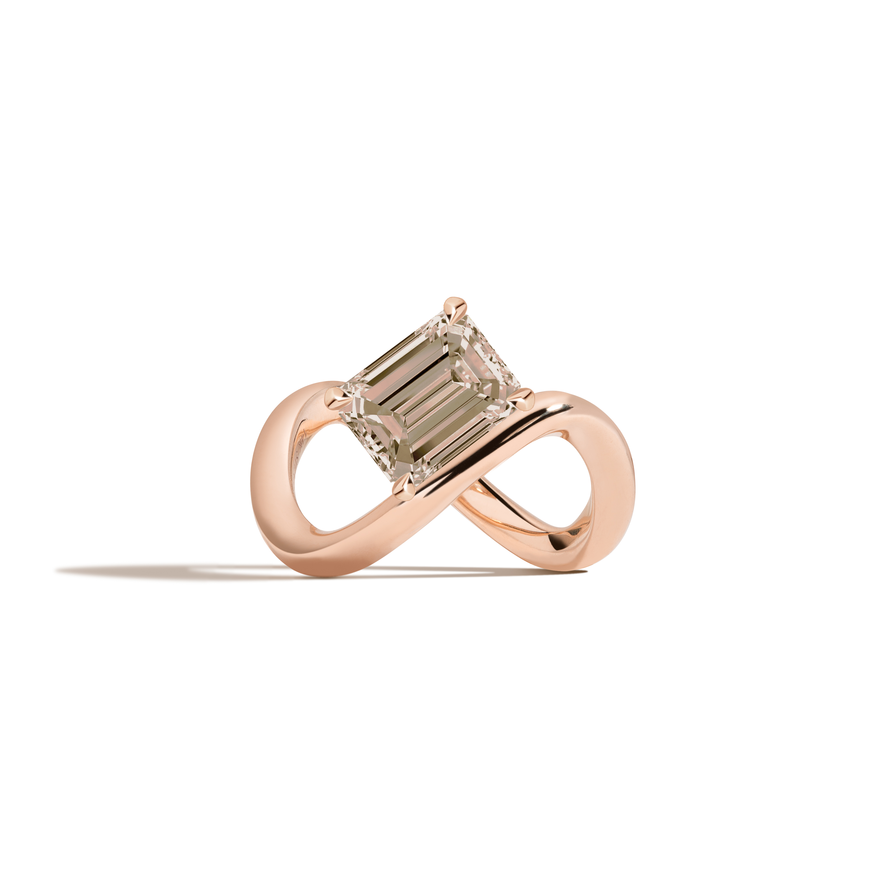 A rose gold infinity-shaped ring featuring a tilted emerald-cut champagne diamond center stone, set against a clean white background with a soft shadow.