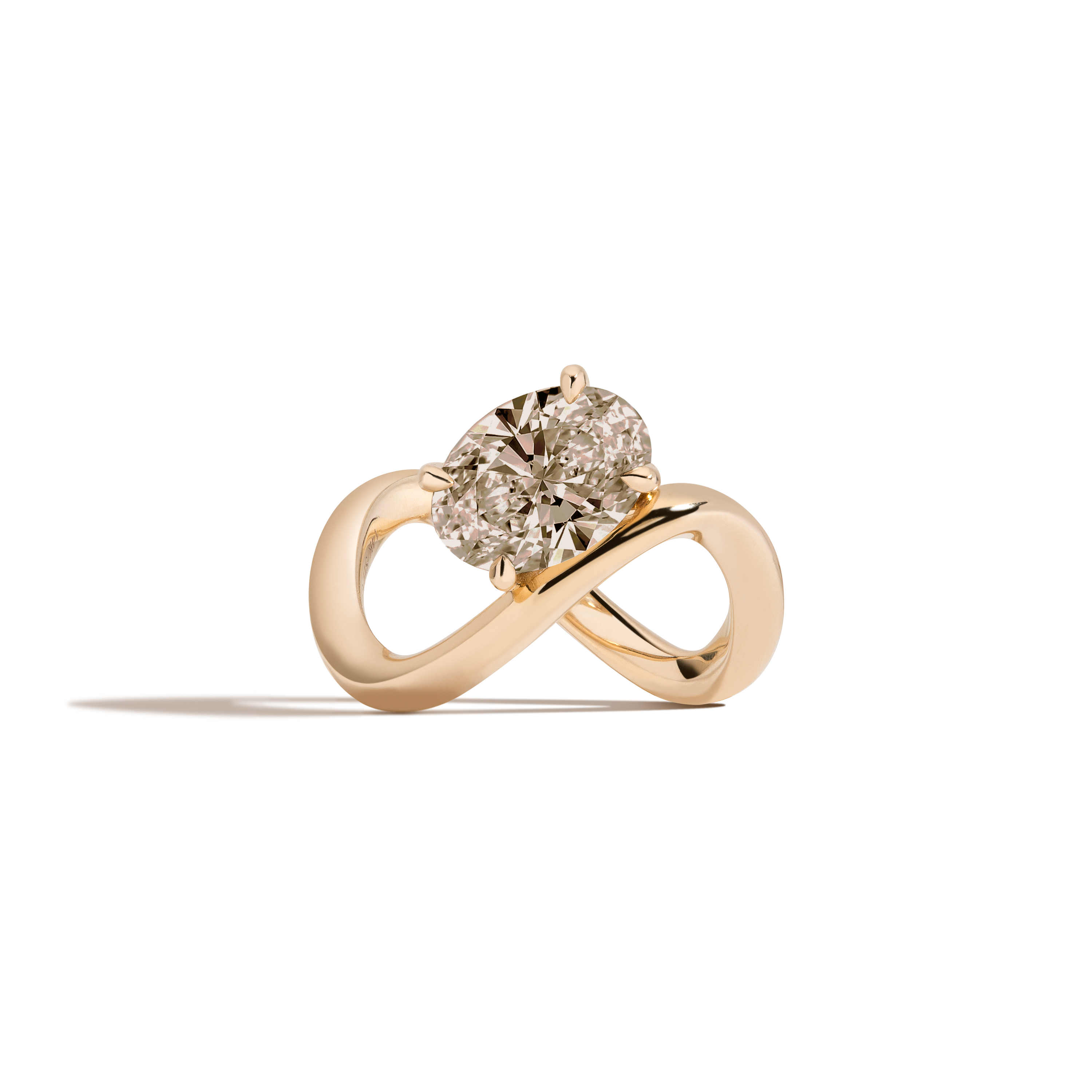 A yellow gold infinity-shaped ring featuring a tilted oval champagne diamond center stone, set against a clean white background with a soft shadow.