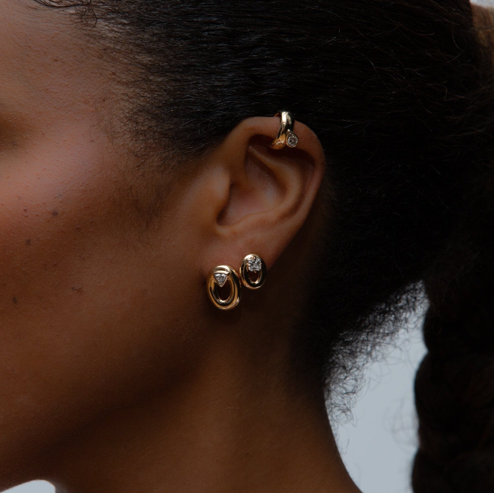 An ear with three yellow gold earrings with diamonds