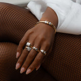 A hand wearing a mix of four rings and a bracelet, all made of yellow and white gold and diamonds
