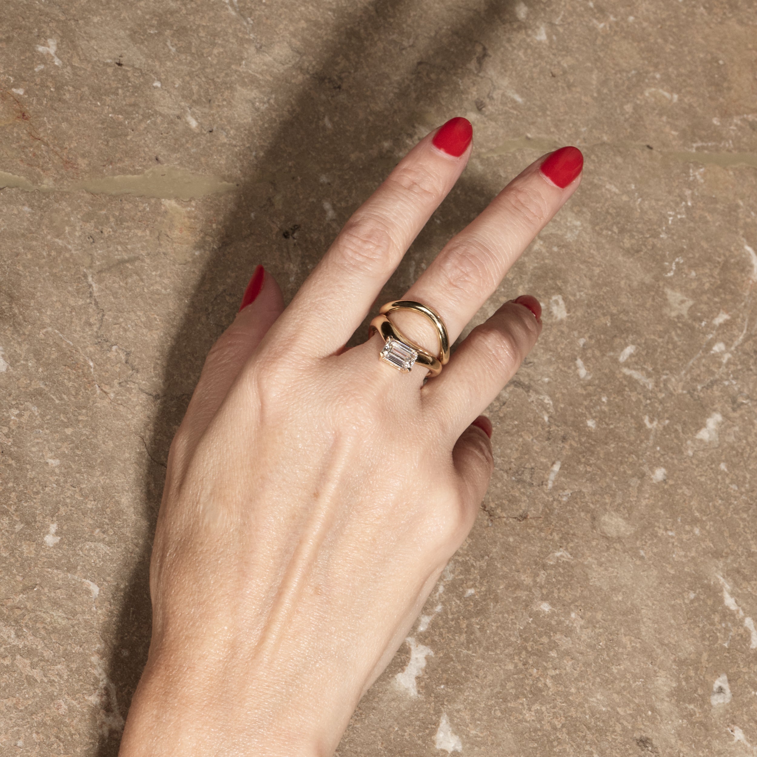 cloud offset emerald ring paired with cloud wedding band on hand with textured background